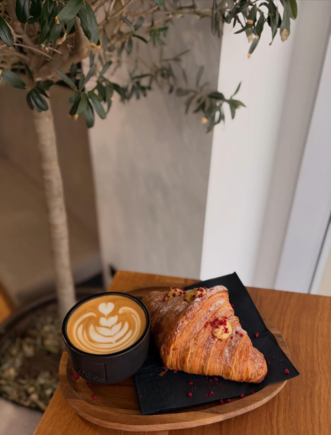 A croissant served beside a latte under an olive tree
